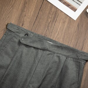 K&ouml;nnte beinhalten: Graue Twill-Hose mit G&uuml;rtelschlaufe und Knopfverschluss. Die Hose hat eine gefaltete Vorderseite und ein gerades Bein.