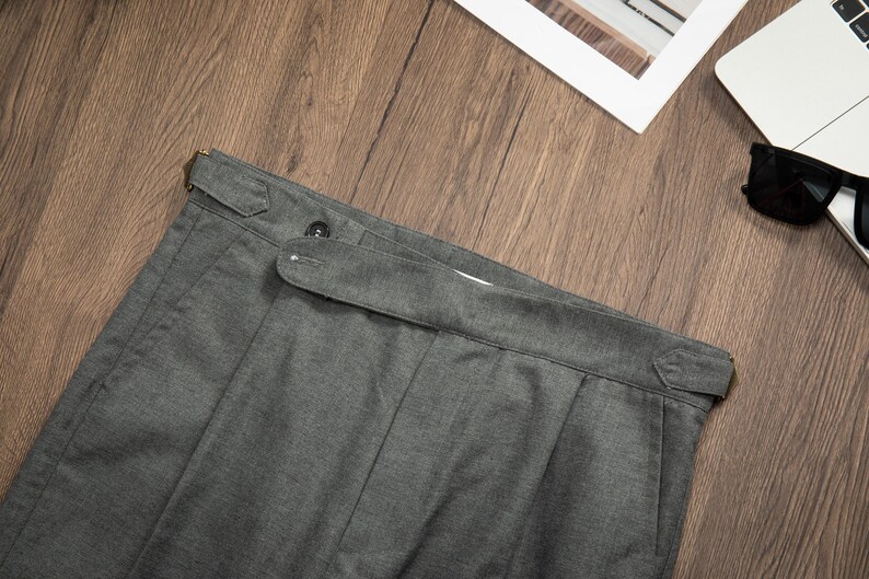 K&ouml;nnte beinhalten: Graue Twill-Hose mit G&uuml;rtelschlaufe und Knopfverschluss. Die Hose hat eine gefaltete Vorderseite und ein gerades Bein.