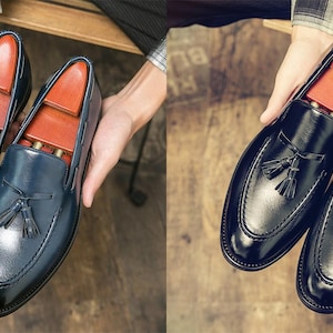 May include: Two pairs of leather tassel loafers, one pair in blue and one pair in black. The loafers have a pointed toe and a tassel detail on the vamp.
