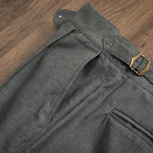 K&ouml;nnte beinhalten: Nahaufnahme einer dunkelgrauen Hose mit einer einzigen vorderen Tasche und einer Messing-Schnalle am Bund.