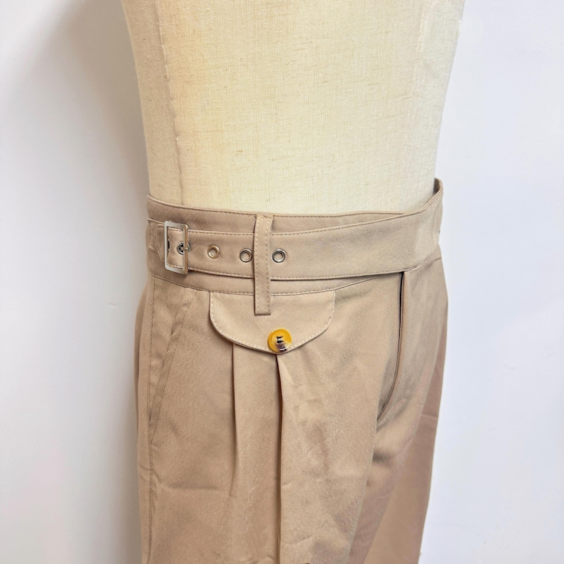 Puede incluir: Pantal&oacute;n beige de cintura alta con cintur&oacute;n y un solo bolsillo con bot&oacute;n. El pantal&oacute;n tiene pliegues en la parte delantera.