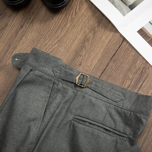 K&ouml;nnte beinhalten: Graue Wollhose mit einer einzigen Ges&auml;&szlig;tasche und einer Messing-Schnalle am Bund.