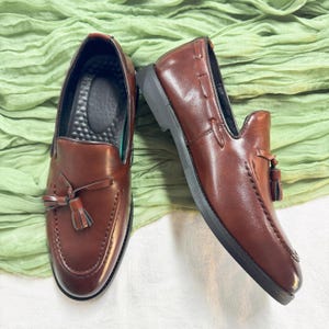 May include: A pair of brown leather loafers with tassels. The loafers have a dark brown leather upper and a black rubber sole.