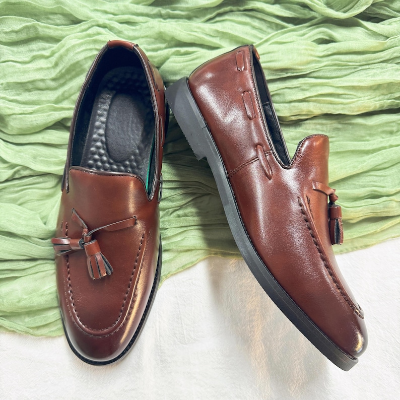 May include: A pair of brown leather loafers with tassels. The loafers have a dark brown leather upper and a black rubber sole.
