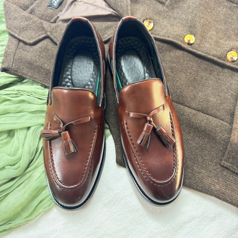 May include: A pair of brown leather tassel loafers with a stitched design. The loafers have a pointed toe and a tassel detail on the front.