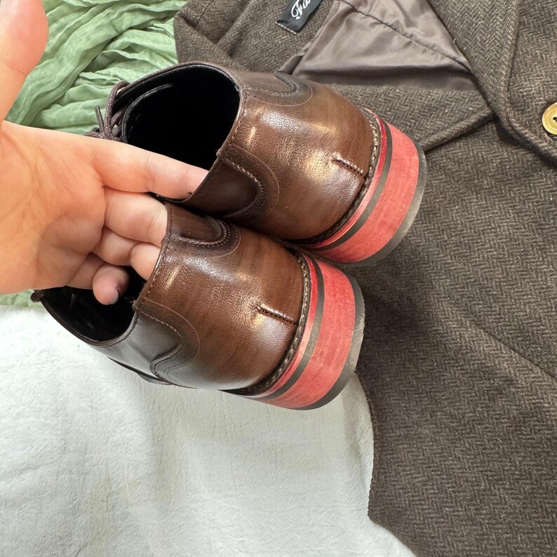 May include: A pair of brown leather shoes with red trim on the soles. The shoes are laced and have a classic design.