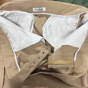 Puede incluir: Primer plano del interior de un pantal&oacute;n beige. El pantal&oacute;n tiene un forro blanco y cierre de cremallera y bot&oacute;n. La cintura tiene una etiqueta que dice "Fashion".