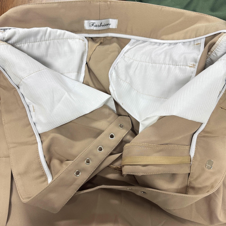 Puede incluir: Primer plano del interior de un pantal&oacute;n beige. El pantal&oacute;n tiene un forro blanco y cierre de cremallera y bot&oacute;n. La cintura tiene una etiqueta que dice "Fashion".