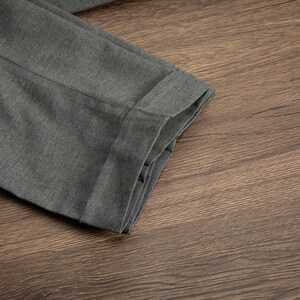K&ouml;nnte beinhalten: Nahaufnahme einer grauen Hose, die in der H&auml;lfte gefaltet ist und die Textur des Stoffes und den Saum zeigt.