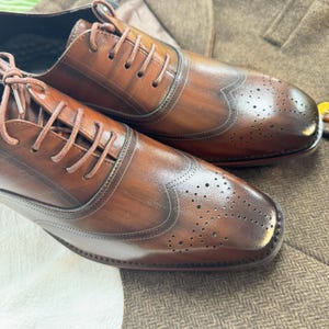 May include: A pair of brown leather oxford shoes with wingtip detailing and a brogue pattern. The shoes have a lace-up closure and a polished finish.