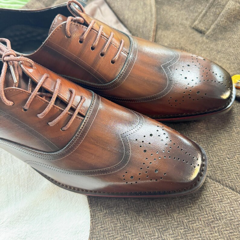 May include: A pair of brown leather oxford shoes with wingtip detailing and a brogue pattern. The shoes have a lace-up closure and a polished finish.