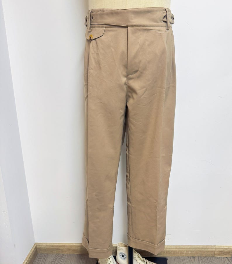 Puede incluir: Un pantal&oacute;n beige de cintura alta con cintur&oacute;n y cierre de bot&oacute;n. El pantal&oacute;n tiene un corte holgado y est&aacute; hecho de una tela ligera.