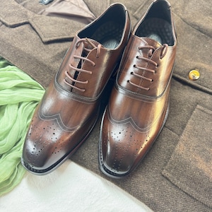 May include: A pair of brown leather lace-up shoes with wingtip detailing and a brogue pattern. The shoes have a polished finish and are made of high-quality leather.