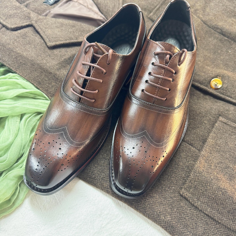 May include: A pair of brown leather lace-up shoes with wingtip detailing and a brogue pattern. The shoes have a polished finish and are made of high-quality leather.