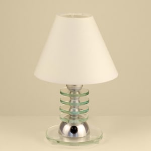 May include: A small, decorative table lamp with a white lampshade. The lamp base is silver with a series of clear, circular glass accents. The lamp has a black on/off switch and a clear glass base. The lamp is a unique home decor item.