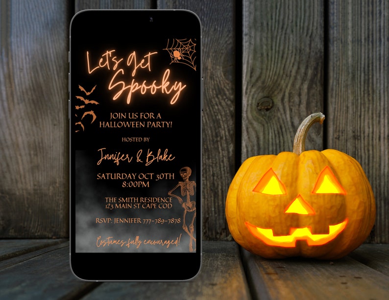 K&ouml;nnte beinhalten: Eine digitale Einladung auf dem Bildschirm eines schwarzen Smartphones mit orangefarbenem Text, der "Let's get Spooky" lautet und Details zu einer Halloween-Party enth&auml;lt. Das Telefon liegt auf einer Holzoberfl&auml;che neben einer beleuchteten K&uuml;rbislaterne.