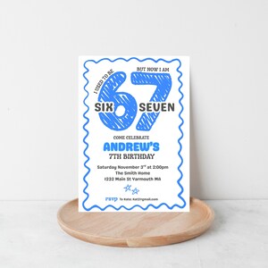 May include: A white invitation with a blue scalloped border. The text reads "I used to be SIX, but now I am SEVEN." It announces Andrew's 7th birthday, with date, time, and location details. The invitation is on a wooden tray.