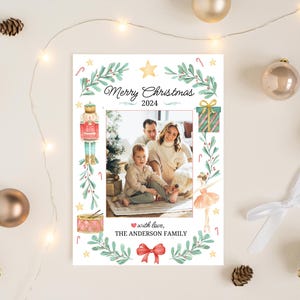 K&ouml;nnte beinhalten: Eine Weihnachtskarte mit einer vierk&ouml;pfigen Familie vor einem Weihnachtsbaum. Die Karte hat ein Aquarelldesign mit einem Nussknacker, einer Ballerina, einer Trommel und einer Geschenkbox. Der Text auf der Karte lautet "Frohe Weihnachten 2024" und "mit Liebe, Die Familie Anderson".