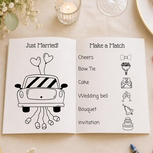 Może przedstawiać: Otwarta książka z aktywnościami weselnymi z napisem "Just Married!" i ilustracją samochodu z balonami w kształcie serca na lewej stronie. Prawa strona zawiera "Make a Match" z ilustracjami i słowami związanymi ze ślubem.