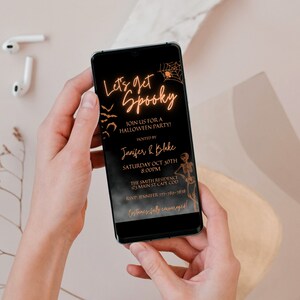 K&ouml;nnte beinhalten: Ein schwarzes Smartphone, auf dem eine Halloween-Partyeinladung mit goldener Schrift angezeigt wird, die "Let's get Spooky" lautet und Details zur Party enth&auml;lt, darunter Datum, Uhrzeit, Ort und RSVP-Informationen.