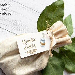 May include: A white gift bag with a brown string tied around it. A white tag with the text "thanks a latte" and a cartoon coffee cup is attached to the bag.