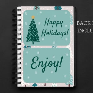 May include: A spiral bound notebook with a white background and a green Christmas tree design. The front cover has two stickers with the text "Happy Holidays!" and "Enjoy!"