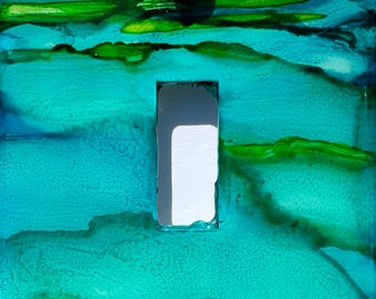 May include: A decorative light switch cover with an abstract design in shades of teal, green, and yellow. The cover features a rectangular opening for the switch and two green, round screw heads.