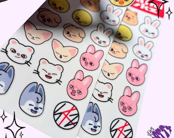 May include: Two sheets of stickers featuring cartoon animal faces, including a bunny, a fox, a cat, a dog, and a pig. The stickers are white with black outlines and are arranged in rows. The sheets are labeled "Mini SKZ" in red and black letters.