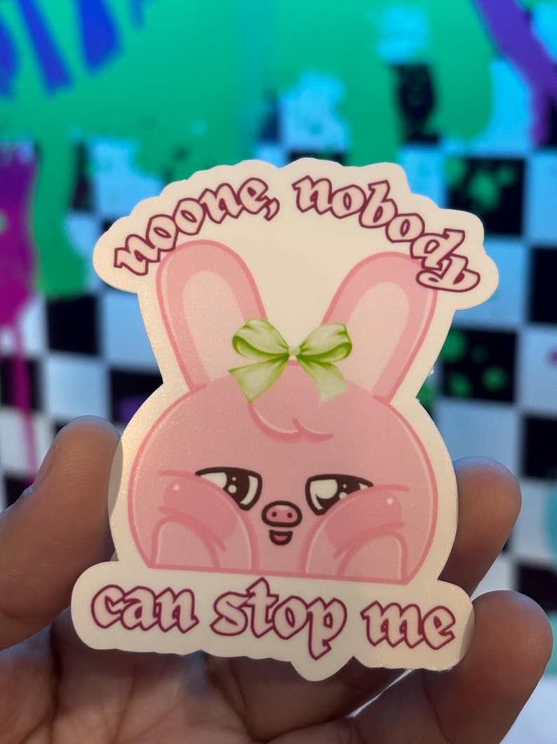 K&ouml;nnte beinhalten: Ein rosa Hasenaufkleber mit dem Text "noone, nobody can stop me". Der Hase hat eine gr&uuml;ne Schleife und eine schweine&auml;hnliche Nase. Der Aufkleber wird in einer Hand gehalten.