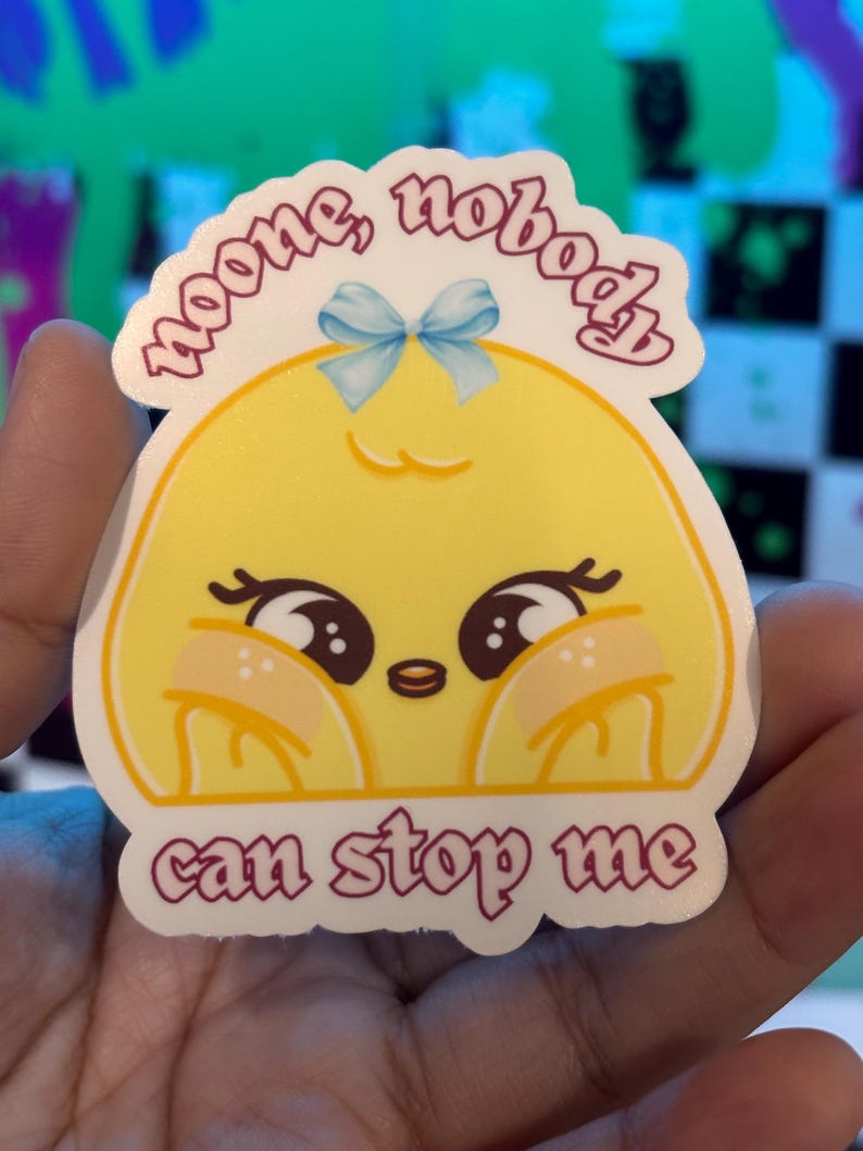 K&ouml;nnte beinhalten: Ein gestanzter Aufkleber mit einer Cartoonfigur mit gelbem Gesicht, gro&szlig;en Augen und einer blauen Schleife. Der Aufkleber hat den Text "noone, nobody" &uuml;ber der Figur und "can stop me" darunter.