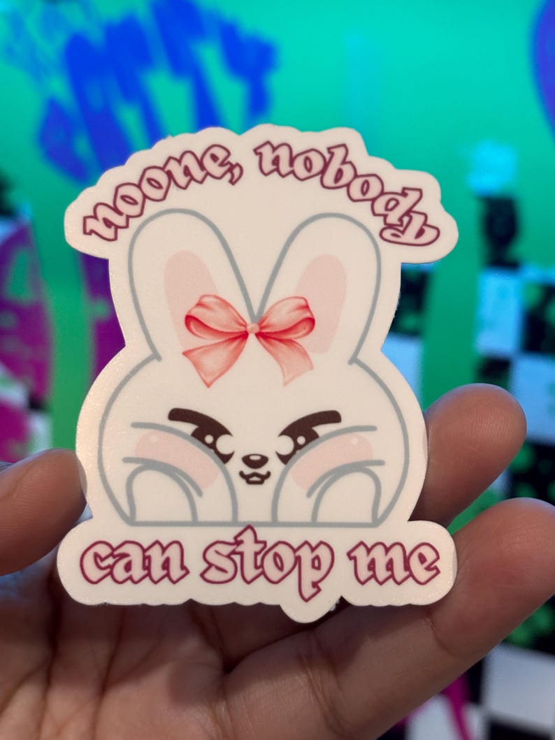 K&ouml;nnte beinhalten: Ein wei&szlig;er Aufkleber mit einem Cartoon-Hasen mit rosa Schleife und rosigen Wangen. Der Aufkleber hat den Text "noone, nobody" &uuml;ber dem Hasen und "can stop me" darunter, alles in Dunkelrosa.