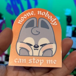 May include: An orange sticker with a cartoon bunny illustration. The bunny is gray with pink cheeks and closed eyes. The sticker has the text "noone, nobody" above the bunny and "can stop me" below.