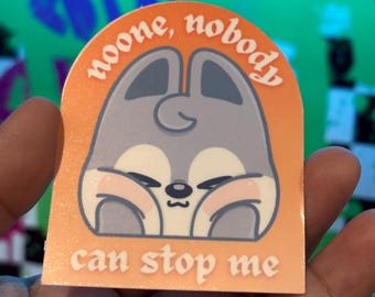 May include: An orange sticker with a cartoon bunny illustration. The bunny is gray with pink cheeks and closed eyes. The sticker has the text "noone, nobody" above the bunny and "can stop me" below.