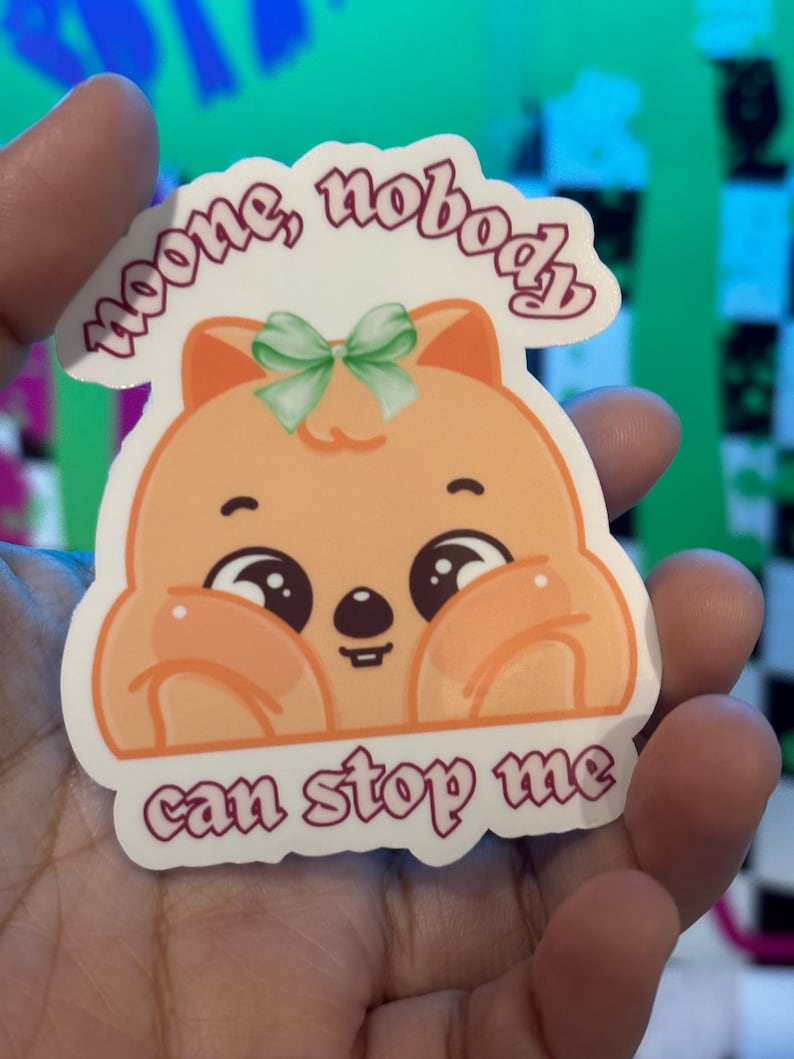 K&ouml;nnte beinhalten: Ein Aufkleber mit einem Cartoon-Quokka mit gro&szlig;en, ausdrucksstarken Augen und einer gr&uuml;nen Schleife. Der Aufkleber hat den Text "noone, nobody can stop me" in einer kursiven Schrift. Das Quokka ist orange und wei&szlig;.