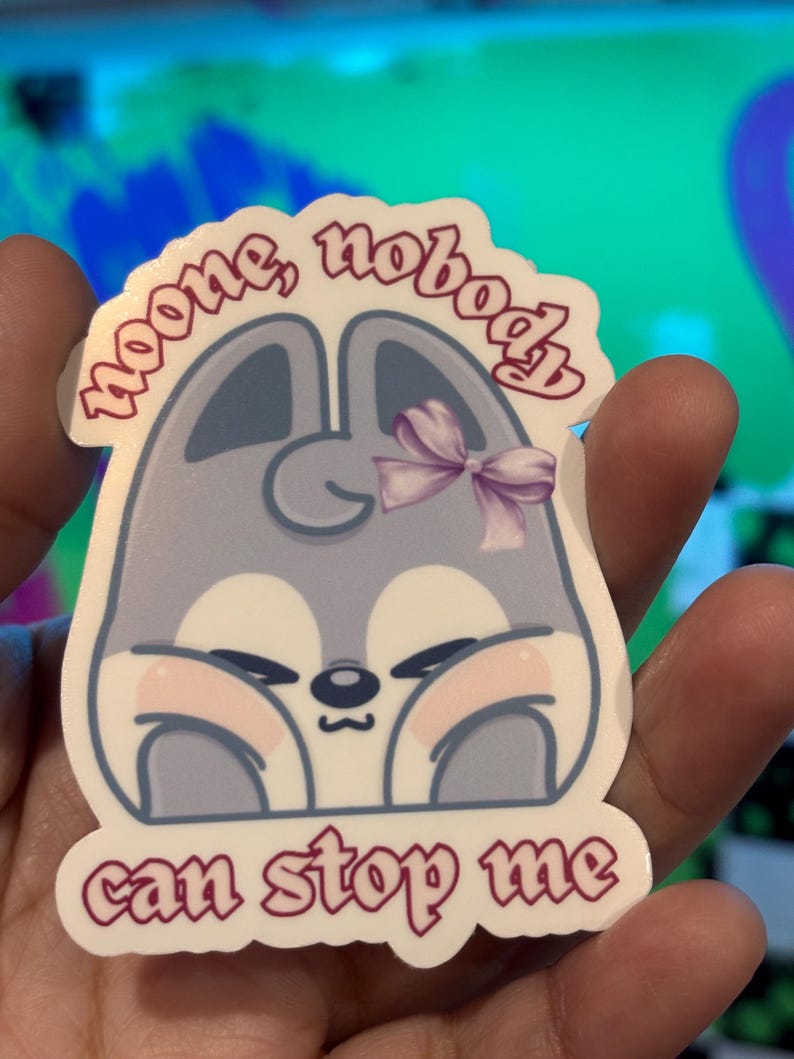 K&ouml;nnte beinhalten: Aufkleber mit einem Cartoon-Tier-Design. Das Tier ist hellgrau mit rosa Wangen und einer lila Schleife. Der Aufkleber hat den Text "noone, nobody can stop me" in rosa.