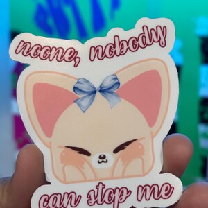 K&ouml;nnte beinhalten: Ein Aufkleber mit einem Cartoon-Fuchs mit rosa Ohren und einer blauen Schleife. Der Aufkleber hat den Text "noone, nobody can stop me" in einer kursiven Schrift. Der Fuchs hat geschlossene Augen und Rouge-Flecken auf den Wangen.
