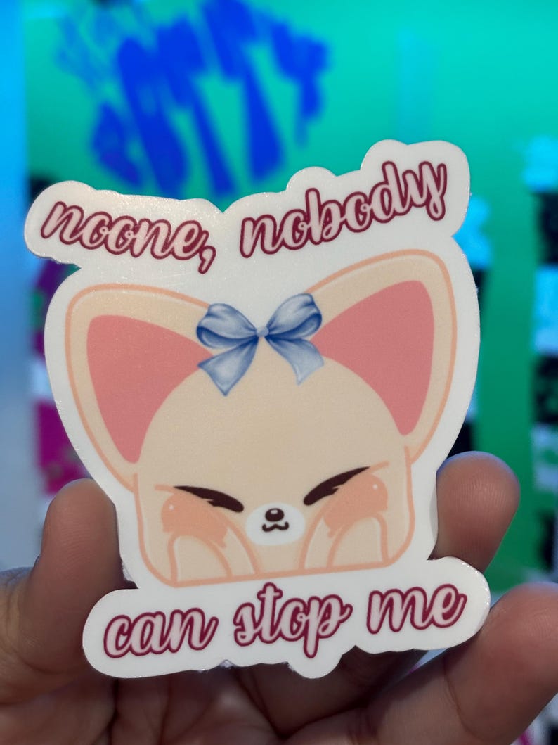 K&ouml;nnte beinhalten: Ein Aufkleber mit einem Cartoon-Fuchs mit rosa Ohren und einer blauen Schleife. Der Aufkleber hat den Text "noone, nobody can stop me" in einer kursiven Schrift. Der Fuchs hat geschlossene Augen und Rouge-Flecken auf den Wangen.