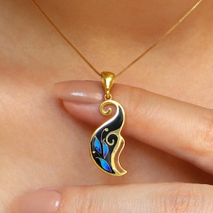 Puede incluir: Un collar de oro con un colgante negro y azul con un diseño floral estilizado.