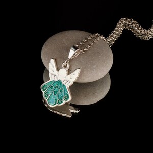 Op de afbeelding: Een zilveren ketting met een groene emaille engel hanger. De engel heeft vleugels en een halo. De ketting ligt op een grijze steen.