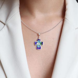 May include: A silver chain necklace with a blue and white enamel cross pendant featuring a floral design. The cross is decorated with white flowers and green leaves.