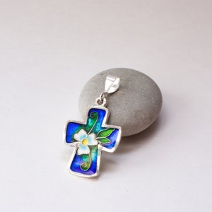 May include: A silver pendant in the shape of a cross with a blue, green, and white enamel flower design.
