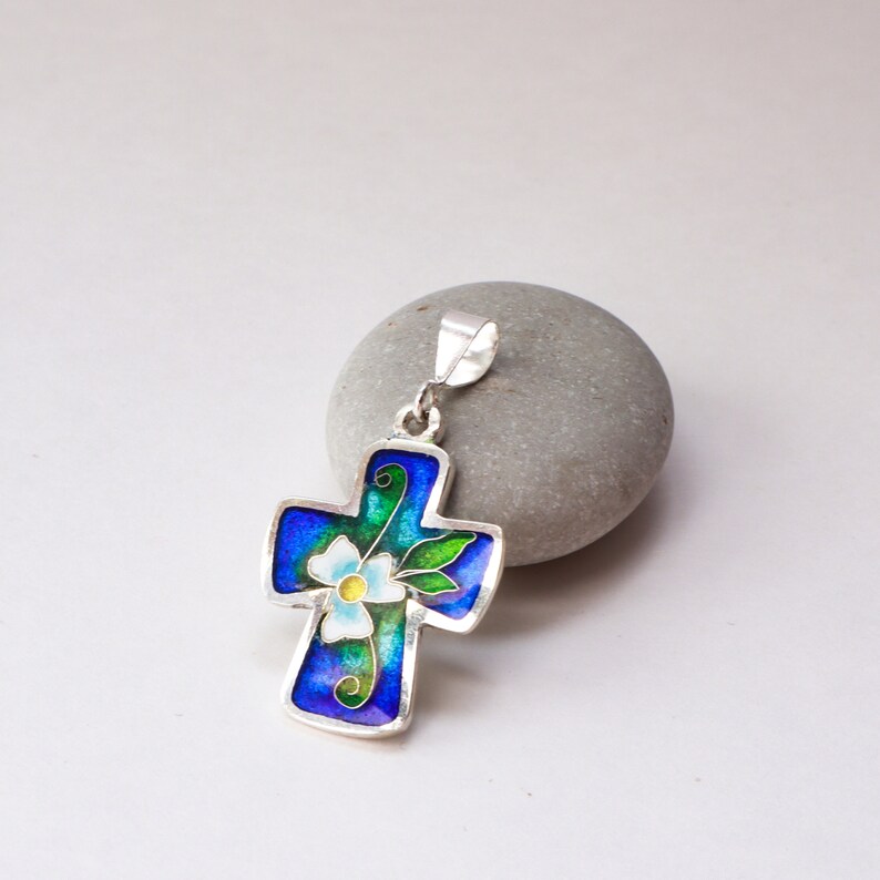 May include: A silver pendant in the shape of a cross with a blue, green, and white enamel flower design.