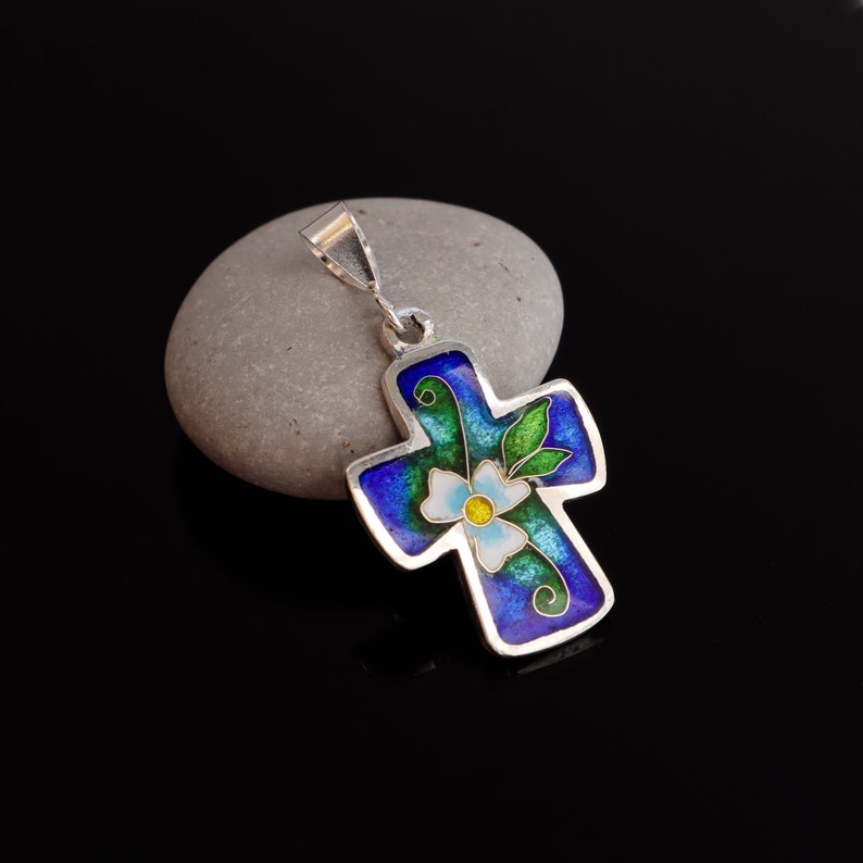 May include: A silver pendant in the shape of a cross with a blue, green, and white enamel flower design.