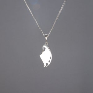 May include: A silver-coloured pendant shaped like a manta ray suspended from a delicate matching silver-coloured chain. The pendant features a smooth, polished surface with cut-out details along the lower edge, creating a distinct silhouette.