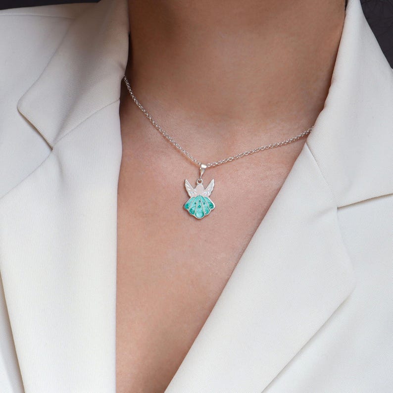 Op de afbeelding: Een zilveren ketting met een groene emaille engel hanger. De engel heeft vleugels en een halo.