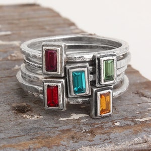 May include: Five silver rings with colorful gemstones. The rings are stacked on top of each other. The gemstones are red, blue, green, and orange.