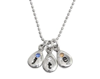 May include: Silver necklace with three teardrop-shaped charms. Each charm has a letter, "j", "t", and "e", and a small gemstone. The gemstones are blue, clear, and orange.