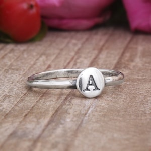 May include: A silver ring with a small oval-shaped charm featuring the letter "A" engraved on it.