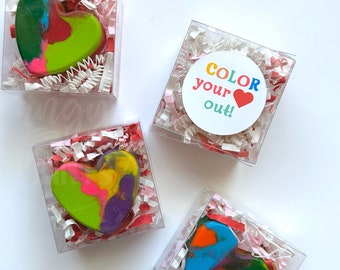 May include: Four small clear boxes with red and white shredded paper inside. Each box contains a heart-shaped crayon made of multiple colors. One box has a round sticker with the text "COLOR your out!" and a red heart.