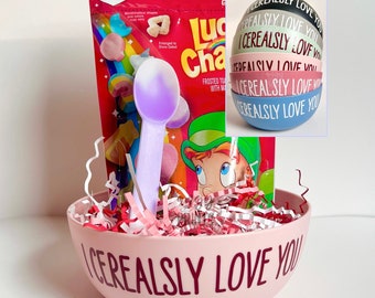 May include: A pink cereal bowl with the text "I Cerealsly Love You" printed on the front. The bowl is filled with pink and white shredded paper and a purple spoon. A box of Lucky Charms cereal and a stack of colorful round stickers with the same text are also in the image.